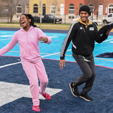 Young Girl in a pink tracksuit skipping and laughing with her coach during a workout outside.